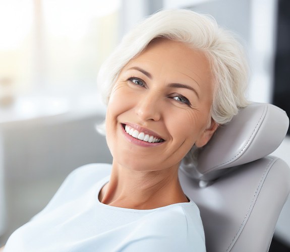 Older woman smiling in treatment chair with dentures 