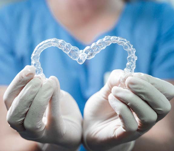 Wilmington Orthodontist holding Invisalign Teen aligners in heart shape