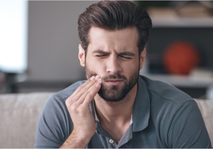 Man in need of emergency entistry holding his cheek in pain
